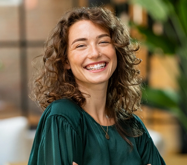 Young woman with curly hair laughing and smiling in an outdoor setting