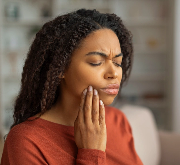 Woman with closed eyes holding her cheek in pain from a dental emergency