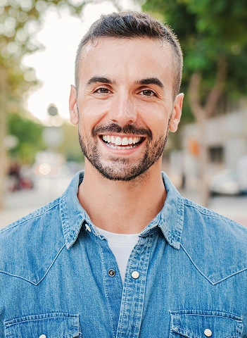 Young man with a beard smiling outdoors in a casual setting