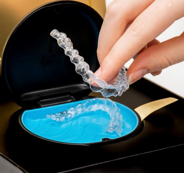 Close up of hands holding a clear Invisalign aligner tray against a dark background