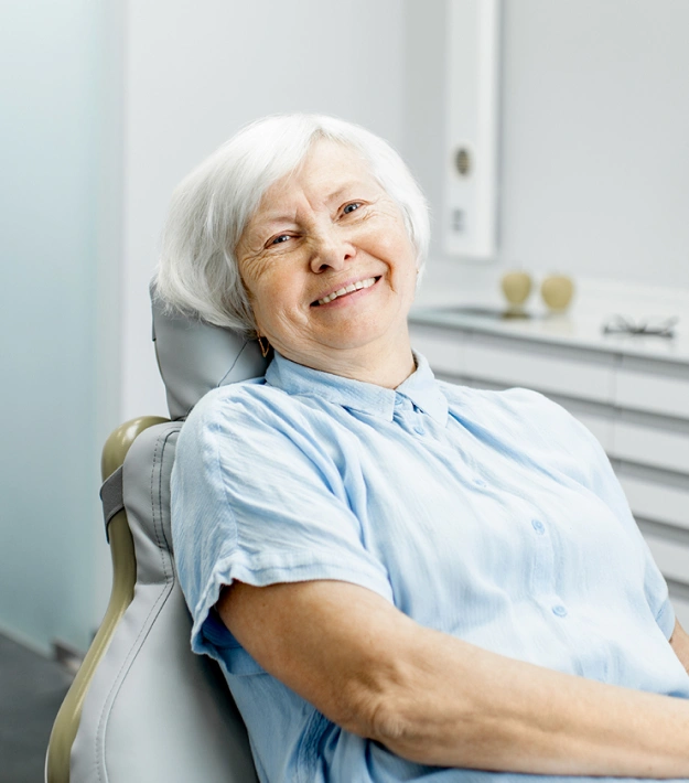 Older woman with white hair smiling while relaxing in a dental chair