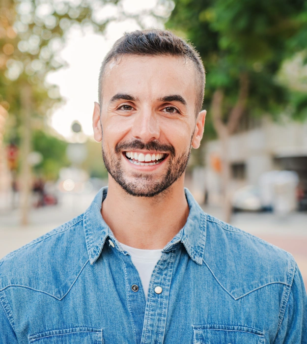 Young man with a beard smiling outdoors in a casual setting