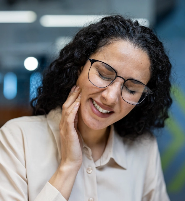 Woman in glasses touching her jaw with a pained expression due to TMJ discomfort